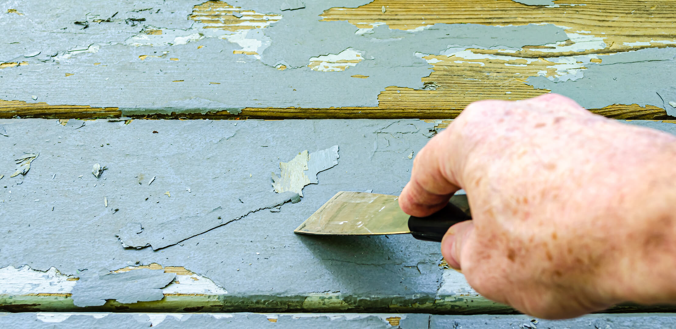 Photo of someone scraping peeling paint on a house