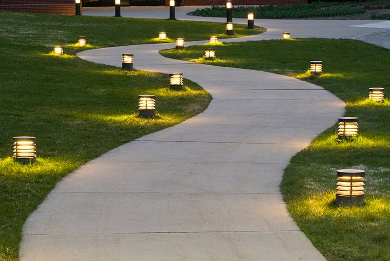 A meandering pathway to a home flanked by green lawn and classy lighting