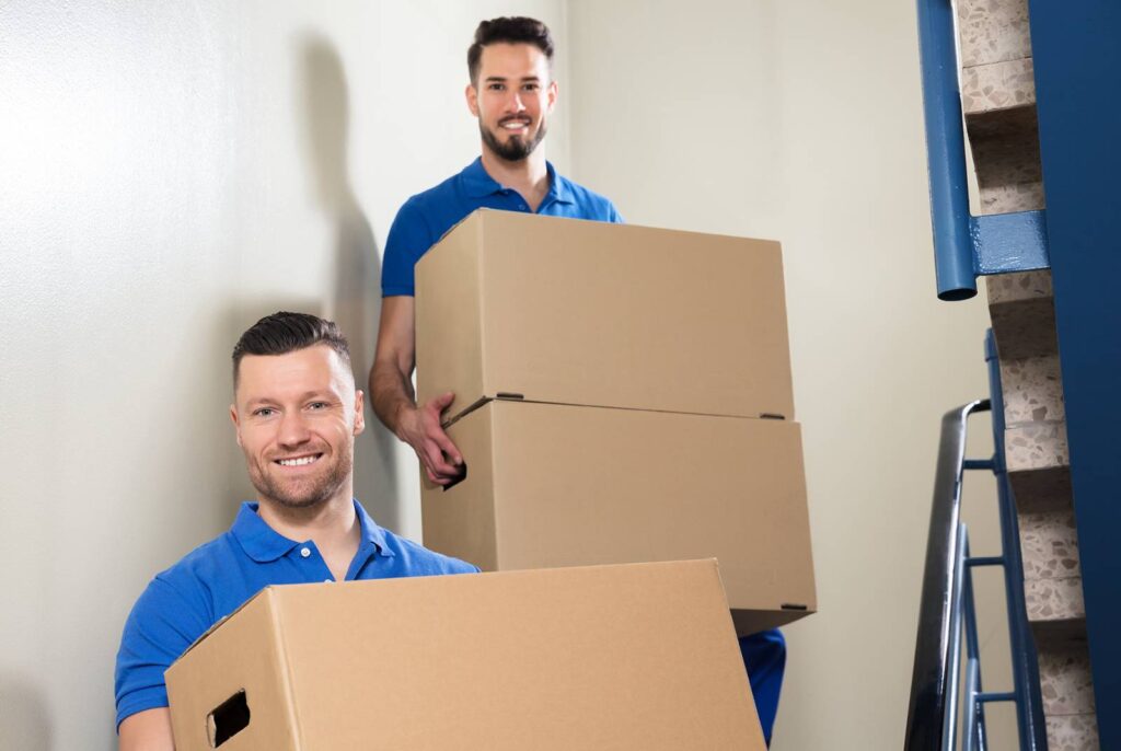 Two young men smiling as they carry boxes down a stairway