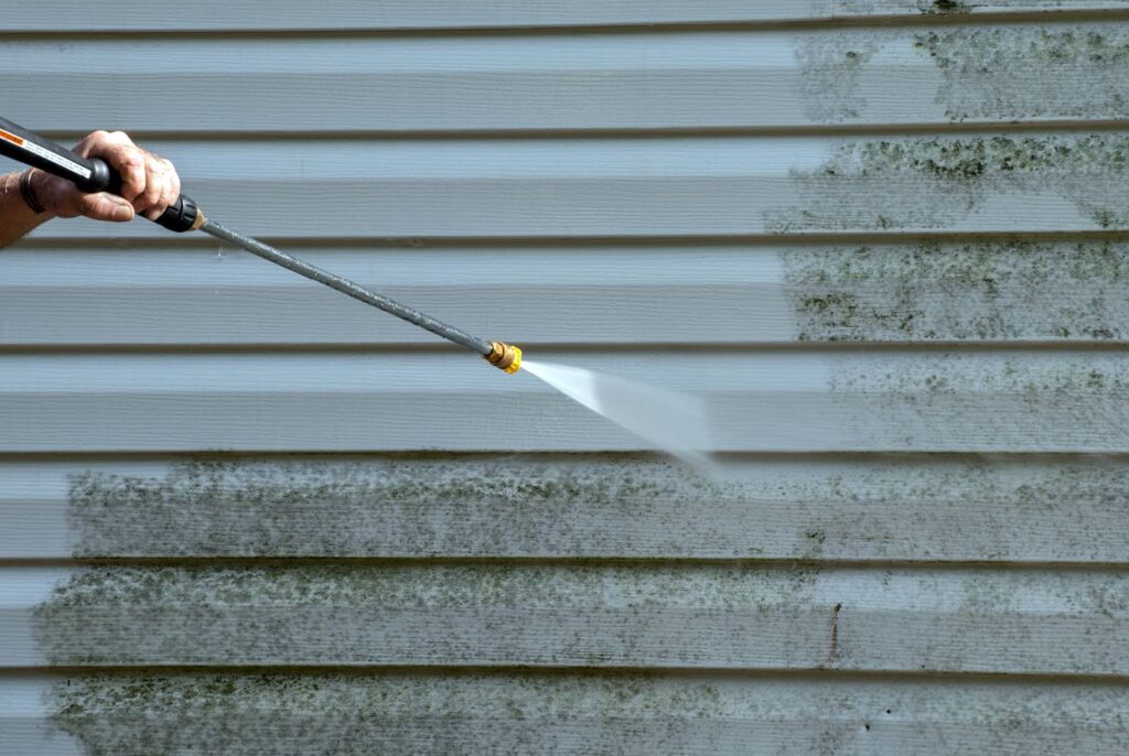 A Get Dwell professional is carefully power washing a home with aluminum siding. Where he has washed is perfectly clean, and the rest of the siding is covered with grime.