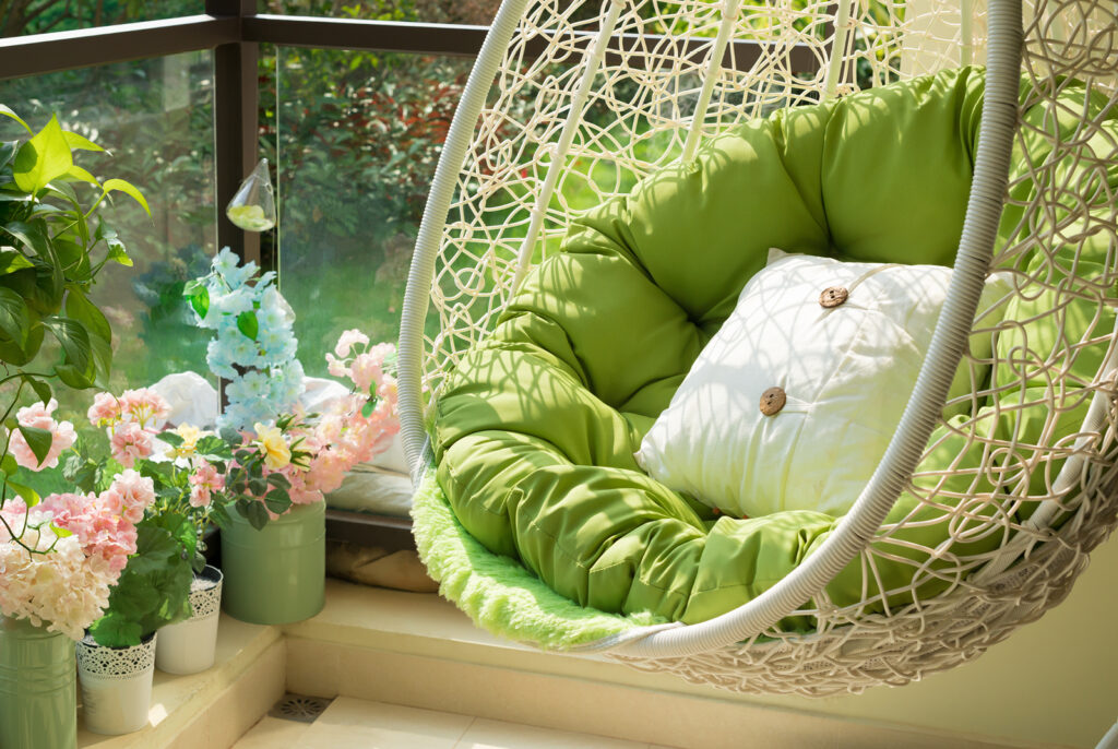 A hanging woven chair on an outdoor porch with beautiful potted flowers