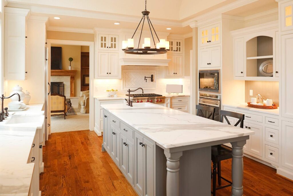 A newly remodeled kitchen with cream colored cabinets and a gray island with marble countertops.