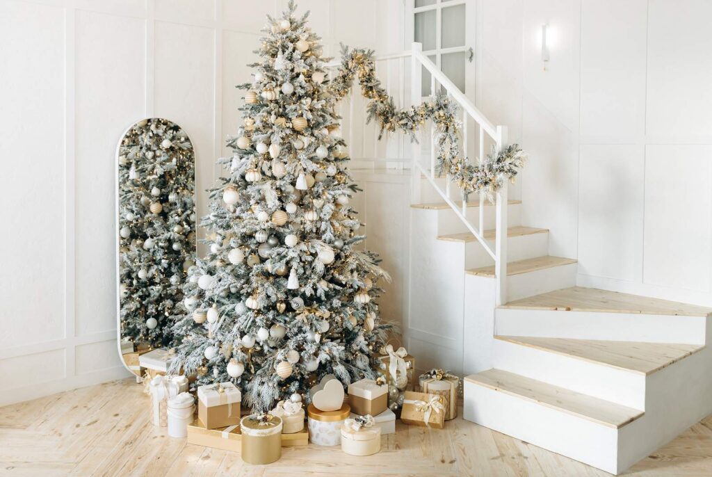 A newly painted entry way with a staircase decked out with a holiday tree, evergreen swag, a mirror and gifts.