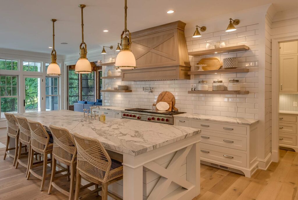 A transitional kitchen with a well curated, layered lighting system — three brass pendants over the island, wall sconces, and small flush mounts on the bottom of open natural wood shelving.