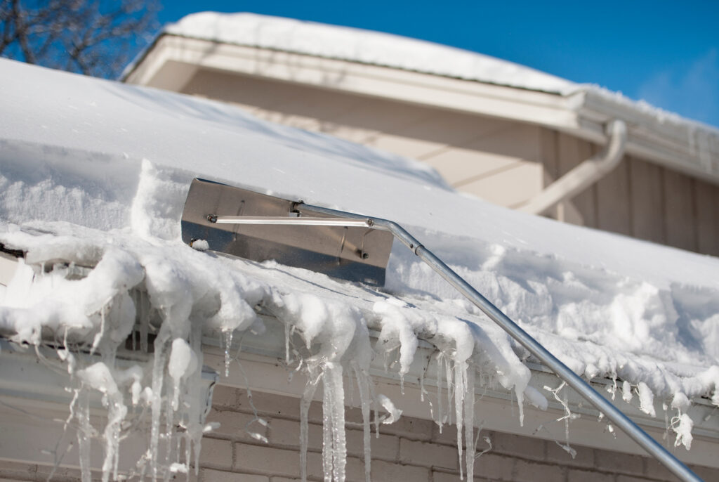 Roof rake being used to clear a snowy roof on a house. 