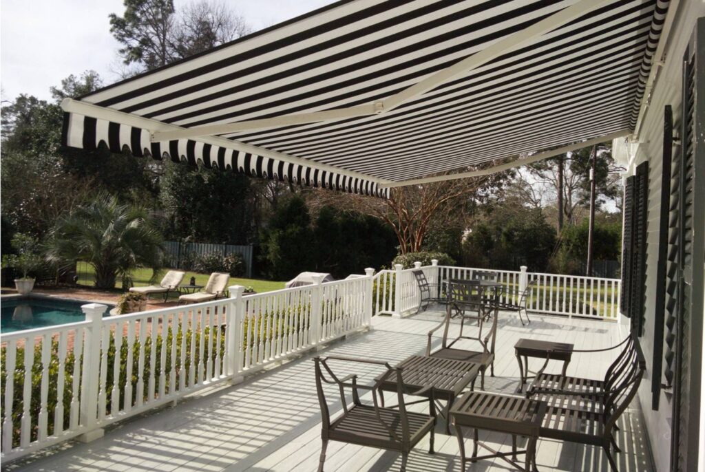 A large custom black and white striped awning spans a high end wooden home deck with a pool in the background