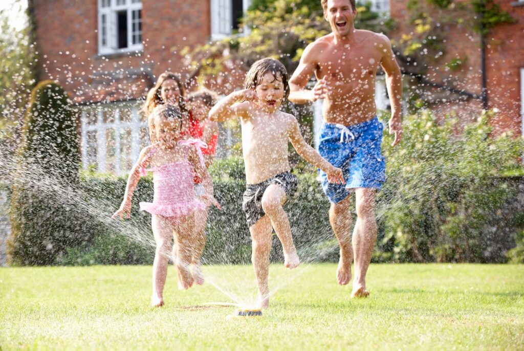 Family of five cooling off by running through a sprinkler in their yard 
