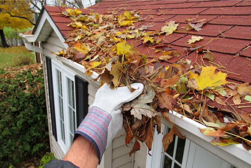 Hand reaching in to a gutter to clear autumn leaves from roof and gutter