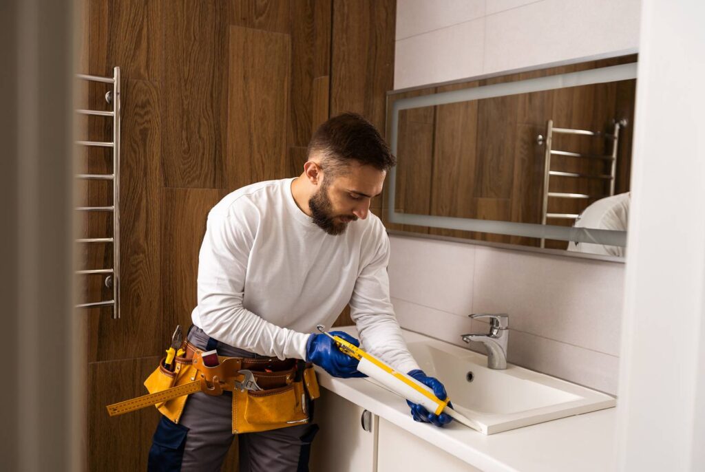 A Get Dwell contractor caulking around a sink during a bathroom remodeling