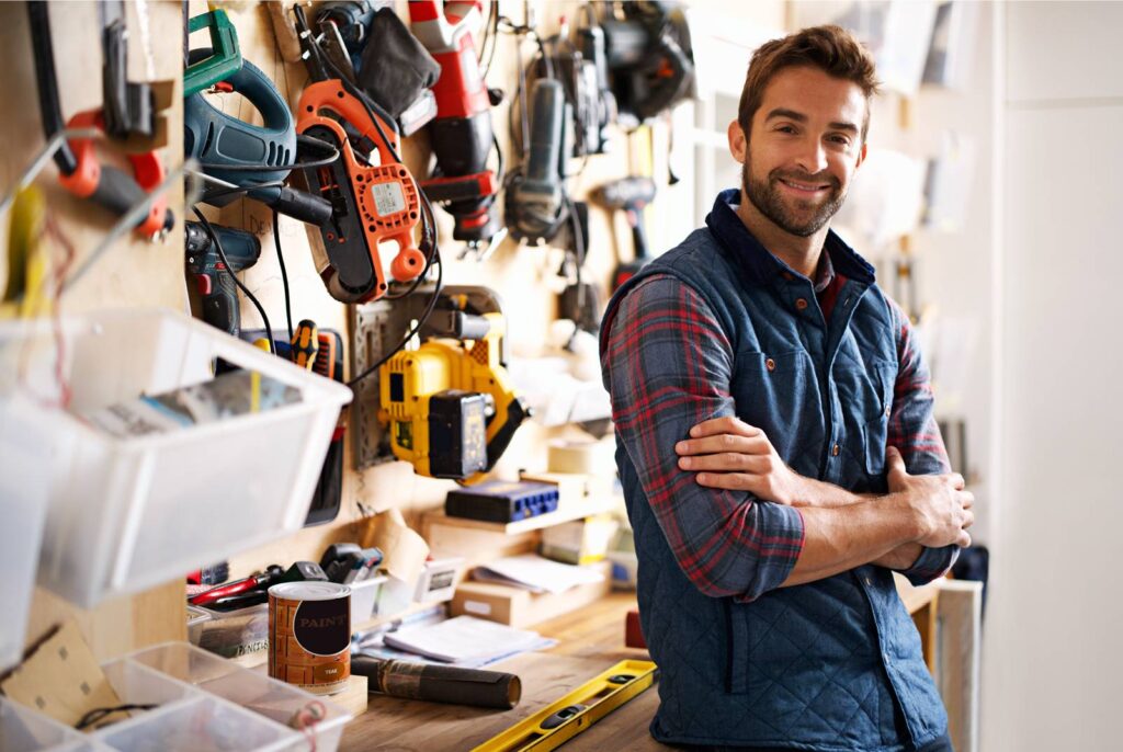 a male DIYer standing with his arms crossed in front of his tools wall