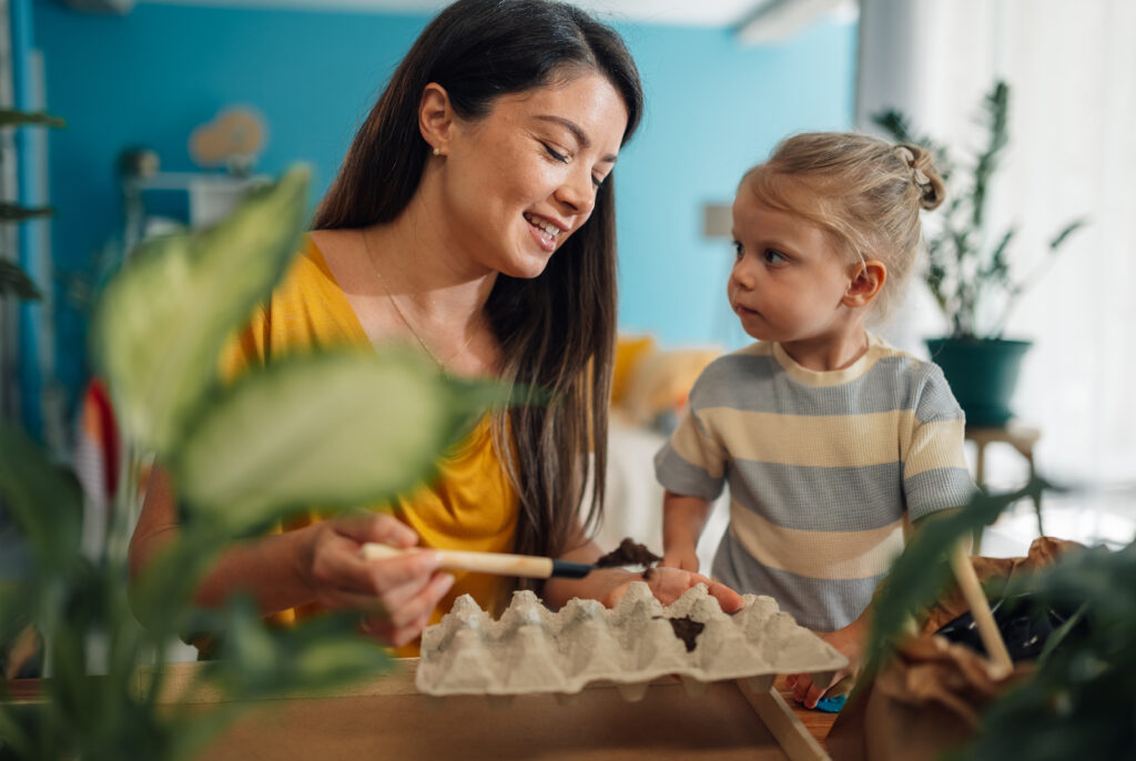 A young woman is teaching her daughter how to plant seeds for their spring garden in egg cartons