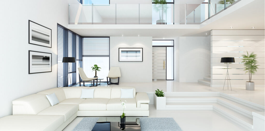 A super modern home interior with white walls, floors, and furniture, a sunken living room with steps down to a huge white wraparound couch, white planters with green plants, a seating area near the windows, modern art on the walls, and a two floor tall ceiling with an overhanging walkway upstairs, glass panels for railings and more green plants. Very dramatic bright lighting floods the beautiful home.