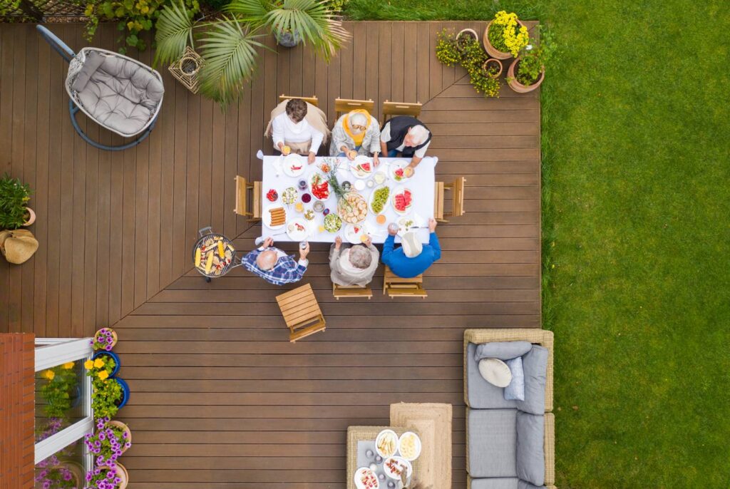 Overhead view of an outdoor summer party on a deck with six people sitting at a table.
