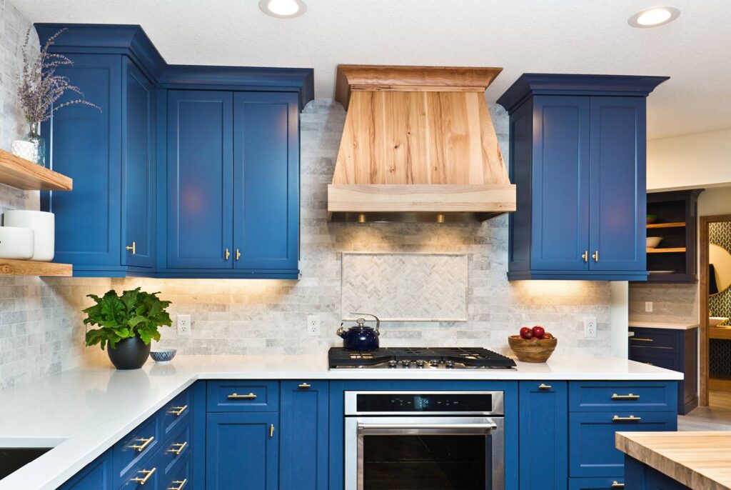 A renovated kitchen with blue painted cabinets and a wooden covered stove hood.
