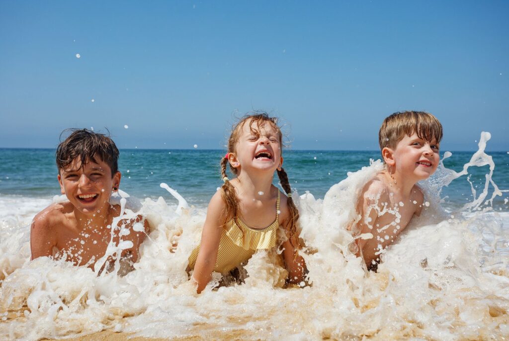 Three small kids smiling with glee as they frolic in the waves one a beach